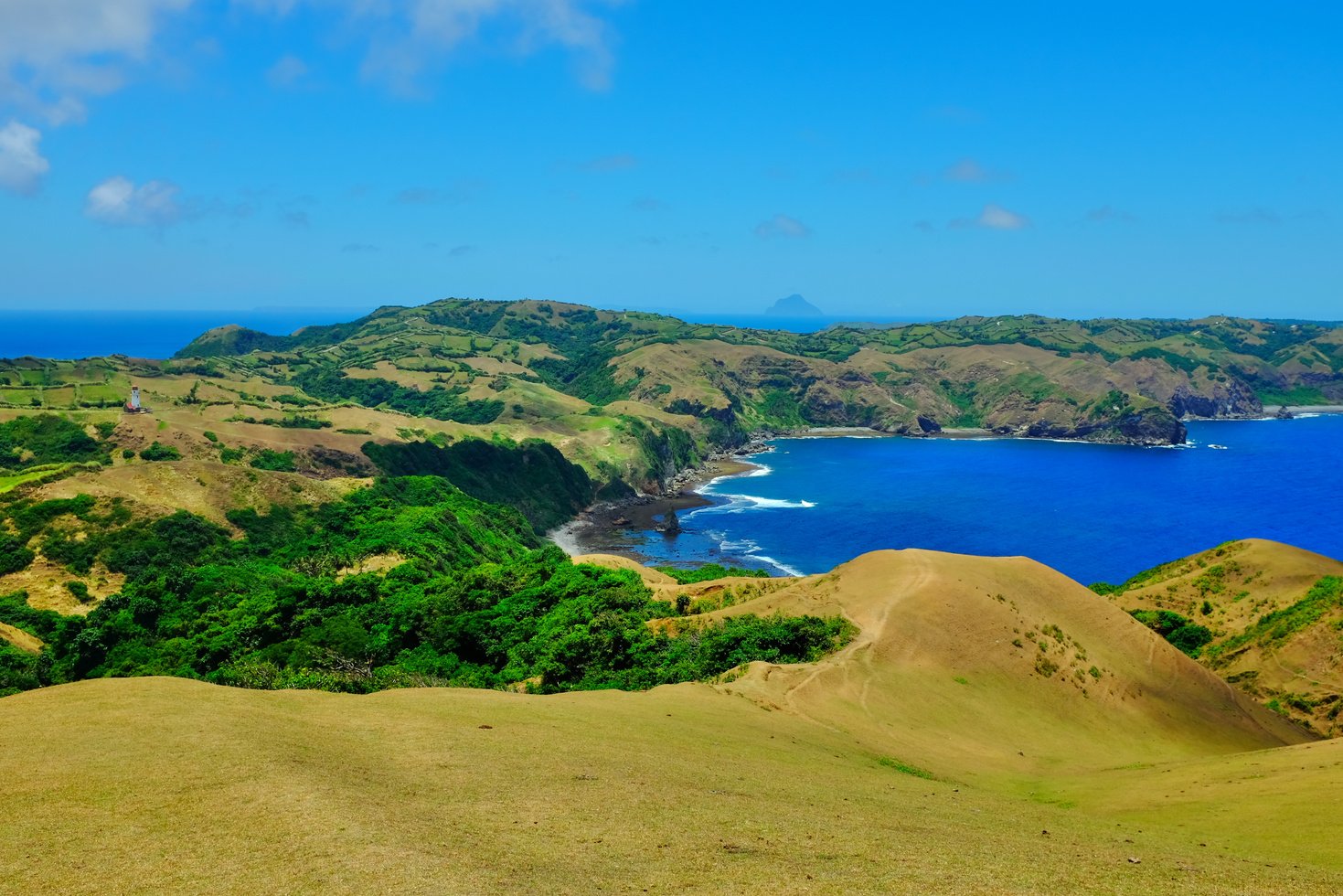 Grass rolling hills, cliffs and blue sea with waves crashing against the shore in Marlboro Country, Batanes, Philippines